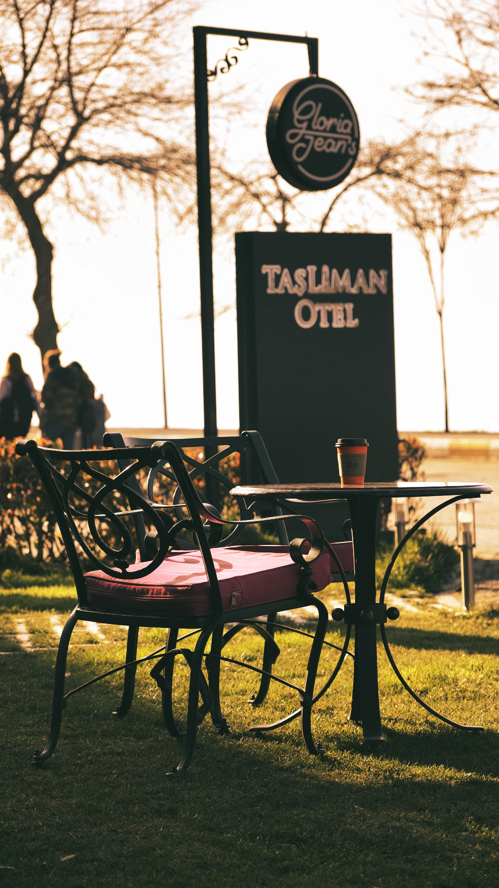 Otel bahçesinde ferforje masada Tchibo kahvesi, arkada Taşliman Otel tabelası